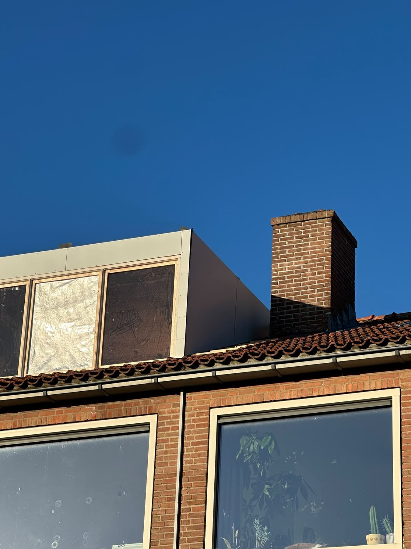 Afgewerkte dakkapel met strakke bekleding naast een gemetselde schoorsteen