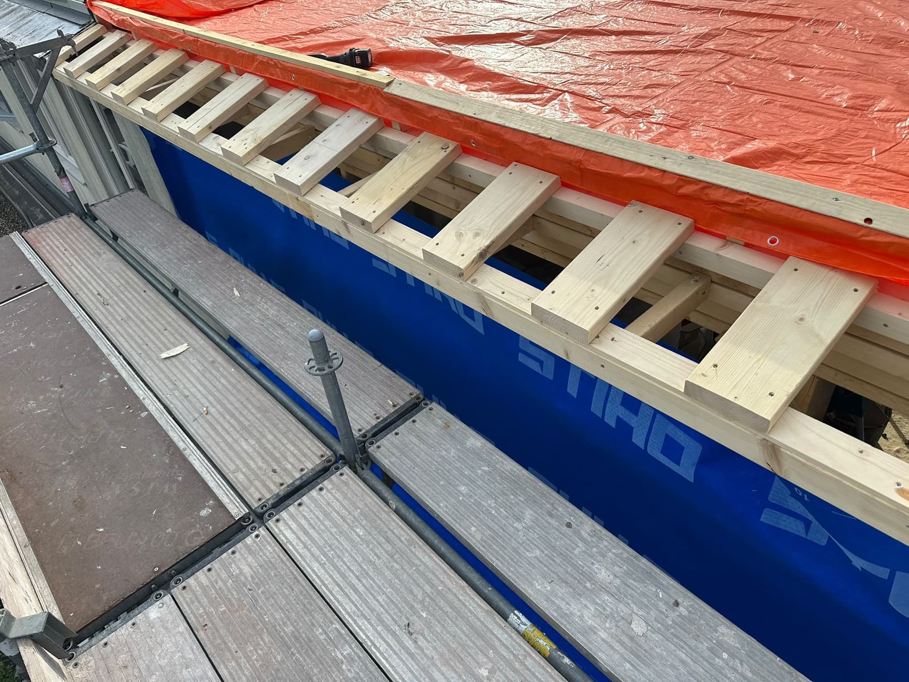 Dakrand met houten overstek in aanbouw boven een dampopen gevelfolie