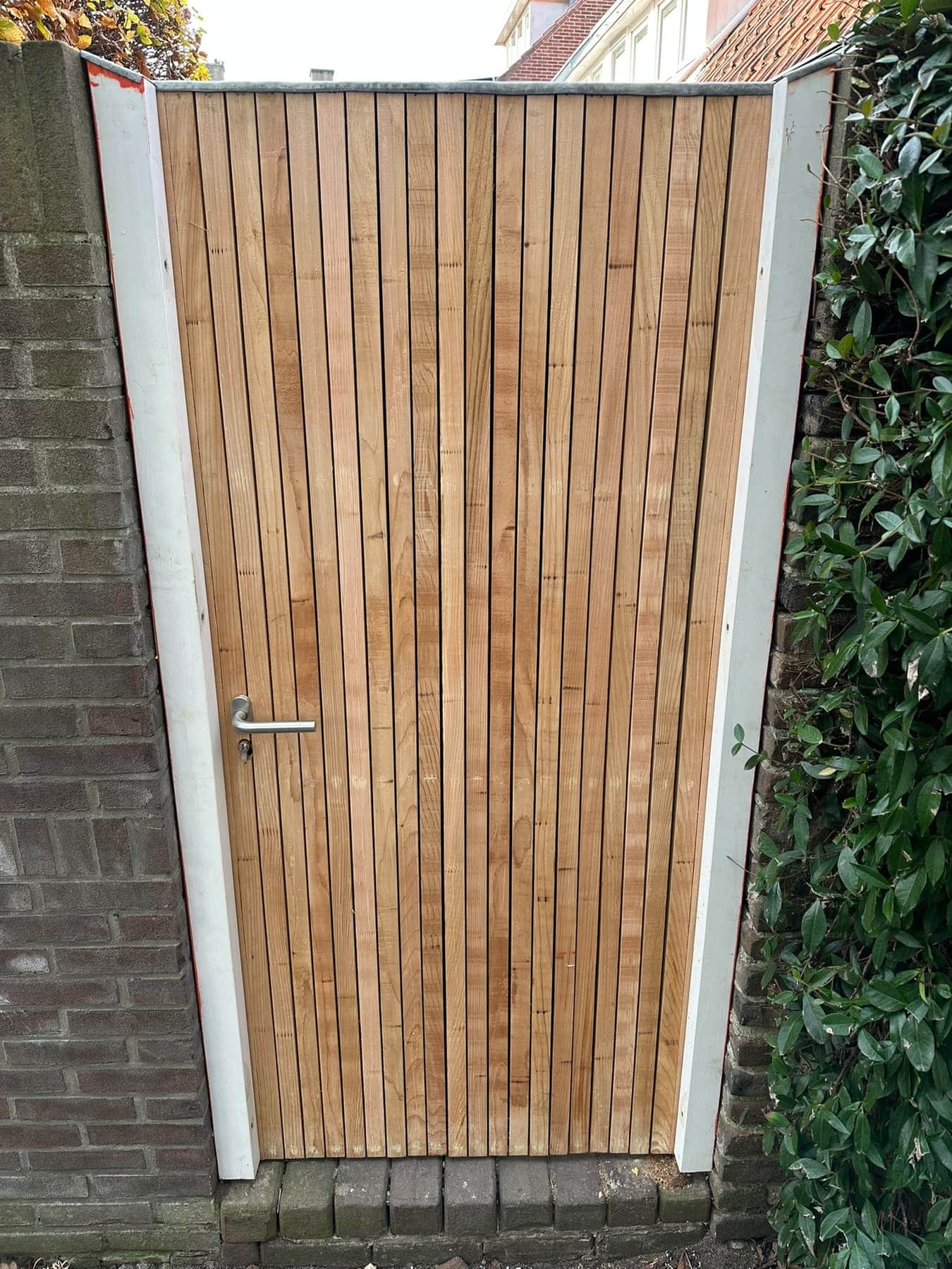 Hardhouten tuinpoort op maat, geplaatst tussen twee gemetselde muren